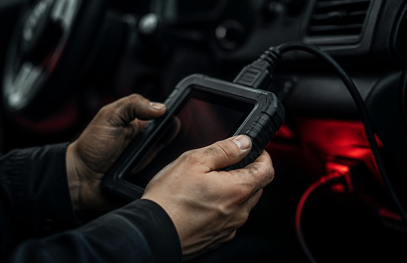 Technician holding a diagnostic scan tool connected to a vehicle's data port.